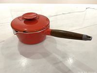 Side view of red sauce pan with wooden handle and lid fitted