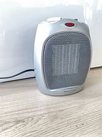 Front view of silver portable heater showing grille, controls and power cord