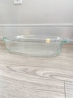 Clear oval Pyrex glass baking dish with side handles on light wood floor