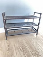 Full view of black three-shelf metal shoe rack on wooden floor