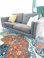 front view of purple two-seat sofa with two pillows on patterned rug