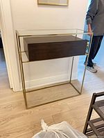 Front view of console table showing glass top, gold frame, wood drawer