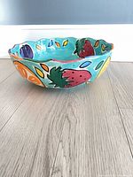Side view showing scalloped ceramic fruit bowl with painted strawberries, oranges, plums on turquoise background