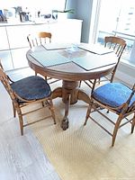 Round wooden pedestal table with three chairs visible, placemats on top