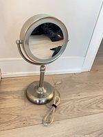 Round magnifying mirror on pedestal with power cord visible