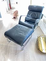 Front view of black leather lounge chair and ottoman on chrome frames