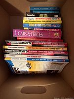 Open box showing stack of 14 automobile price and buying guide books; spines visible identifying multiple Consumer Reports guides, VMR price guides, Edmunds guide.