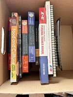 Box containing assorted books and spiral notebook with spines visible