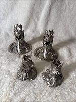 Two pewter iris candlestick holders and two matching pewter salt & pepper shakers on white cloth