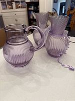 Purple glass pitcher and two ribbed vases