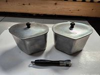Two aluminum triangular pots with lids and one handle displayed