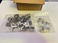 sealed bag of nickel finish mounting plates beside sealed bag of screws and plastic caps with cardboard box behind