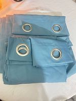 Folded light blue curtain panels showing silver grommets