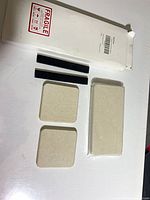 Box with set contents laid out: two black adhesive strips, two square trays, one sealed rectangular tray visible