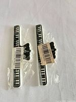 Two identical piano keyboard hair claw clips in clear plastic wrap, barcode stickers visible.