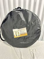Circular dark grey carry bag containing folded tent with instruction label