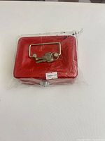 Red metal cash box sealed in plastic with keys on handle front view