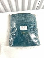 Sealed package containing teal waffle-knit fabric item with barcode label