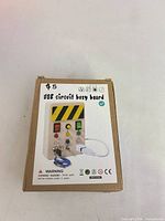 Front of box showing image of USB circuit busy board with buttons, switches, caution stripe and USB cable