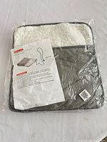 Front of packaged foot warmer showing gray exterior, white sherpa lining, instruction sheet inside plastic