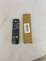 Remote in plastic wrap beside cardboard box, full view of buttons