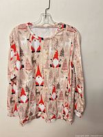 Front view of beige long-sleeve top with gnome and reindeer print on hanger