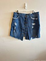 Front view of medium blue distressed denim skirt with button front, ripped areas, frayed hem