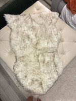 Full view of cream and light brown speckled faux fur throw laid out on ottoman