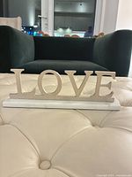 Front view of silver metal LOVE sculpture on white marble base