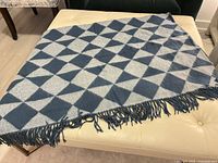 Full view of folded blue and grey diamond-pattern throw blanket on ottoman