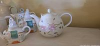 Round white teapot with pink floral motif beside novelty animal-shaped pot