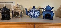 Row of teapots with warmers in navy, cream and blue floral patterns