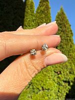 Close-up of both diamond studs held between fingers against outdoor background