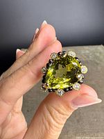 Front view of ring held between fingers showing pear-cut peridot and surrounding stones