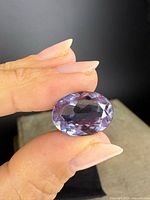 Front view of oval faceted amethyst held between fingers