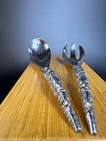 Spoon and fork standing on edge of wood surface showing full handles and utensil heads