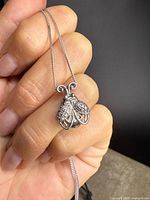 Close-up of sterling silver ladybug pendant held between fingers