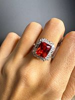 Ring on hand showing size, red center stone, clear halo