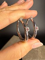 Pair of sterling silver hoop earrings held to show bezels with rubies