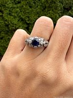 Ring on hand showing sapphire center and clear side stones