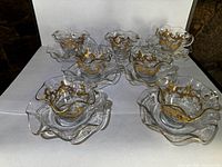 Seven teacups nested in seven saucers showing scalloped rims and gold decoration