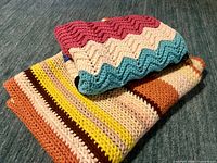 Both afghans stacked showing stripe and ripple patterns
