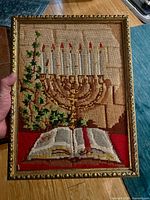 Full view of framed needlepoint showing menorah, candles, book and frame