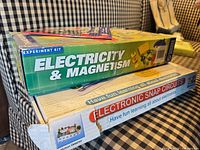 Side view of Electricity & Magnetism kit atop Electronic Snap Circuits box showing torn corner