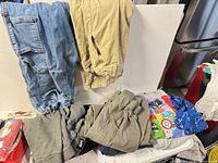 Assorted children’s clothing pieces arranged on table showing denim jeans, khaki pants, grey sweatpants, Marvel tee