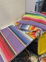 Stack of multicolor serape runners showing weave and frayed edges