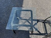 Top view of one glass side table showing square glass top, metal X-frame