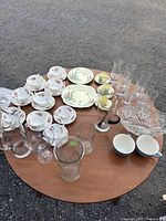 Wide view of entire lot on round table showing variety of china, glassware, and crystal bowl