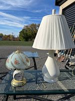 Two table lamps on glass table: floral glass dome lamp with clock and white textured lamp with shade