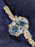 Close-up of oval blue lab diamond centre stone with prongs and accent diamonds on shank